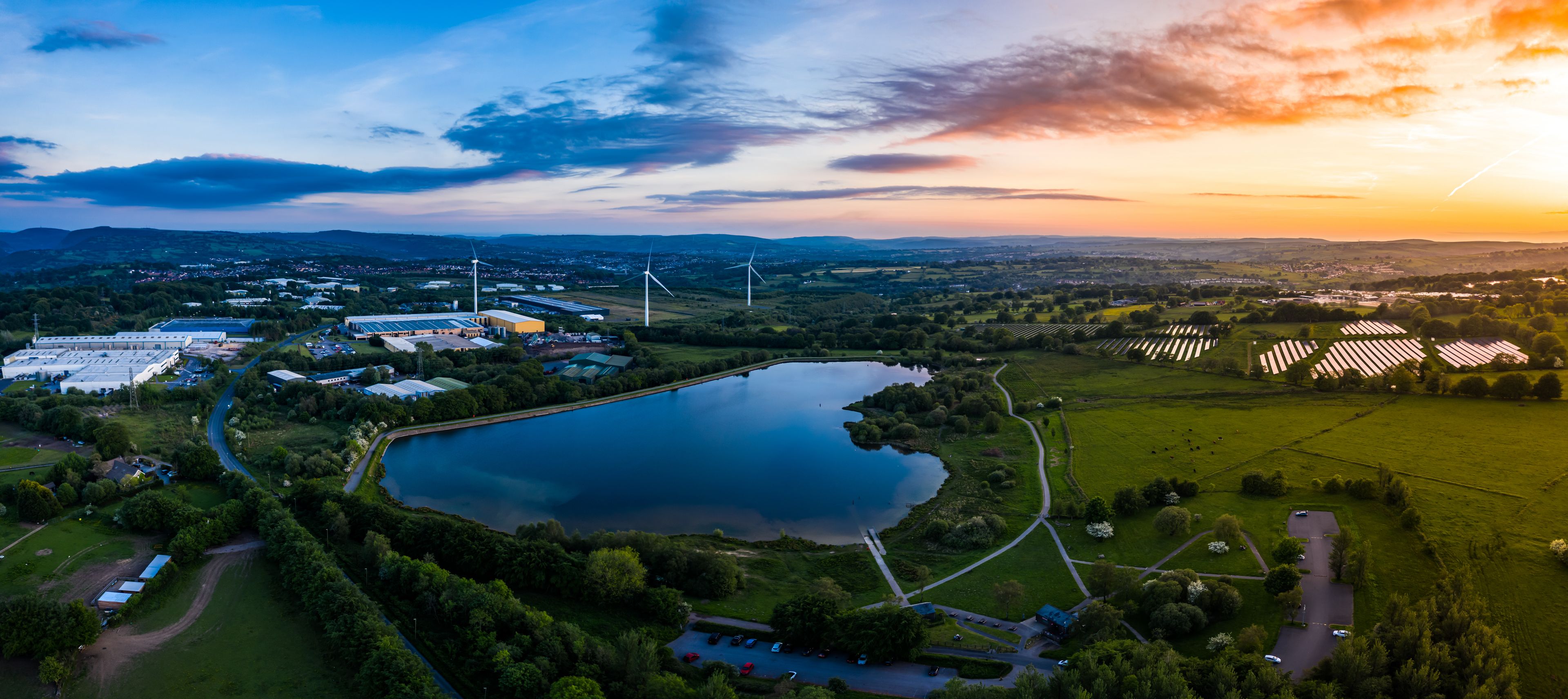 A landscape with a large body of water, wind turbines, and solar panels.