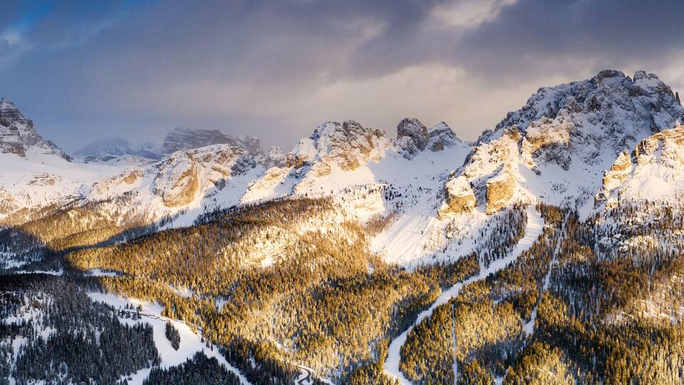 Snow-covered mountains with a forested valley and a clear sky.