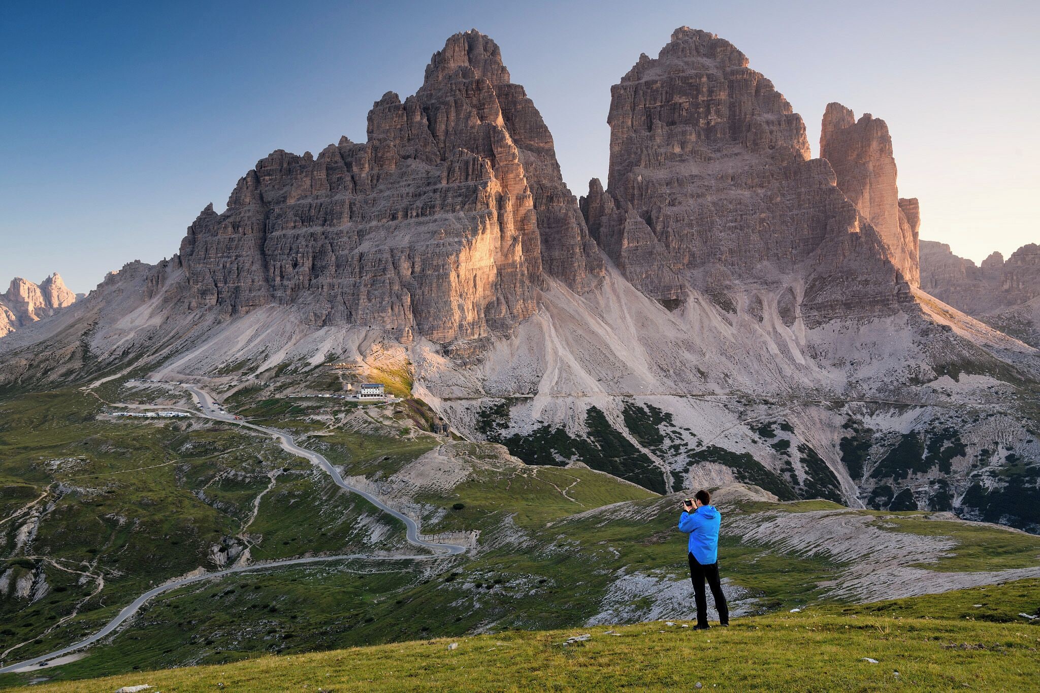 A mountainous landscape with a winding road and a person taking a photo.