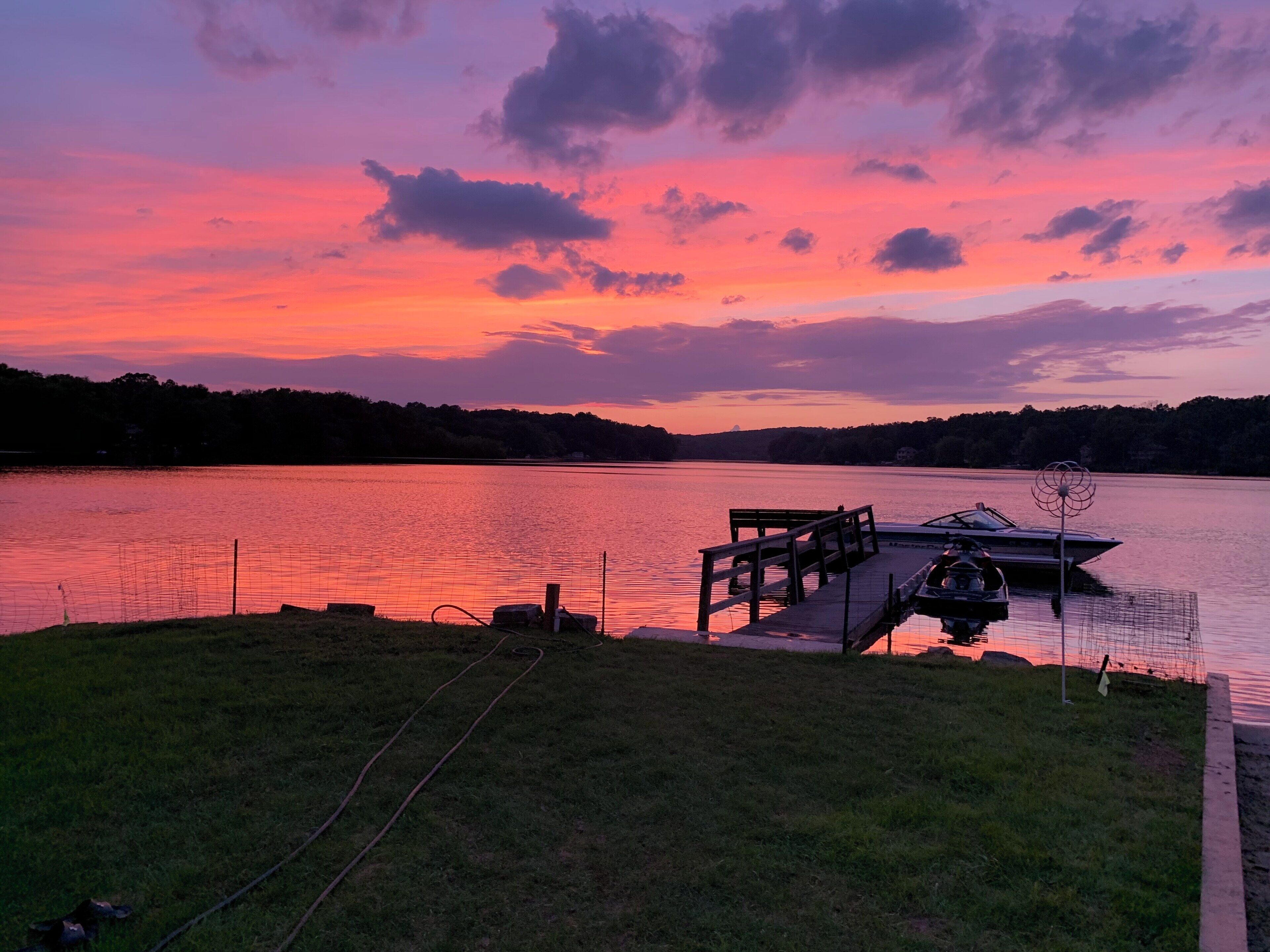 A sunset over a lake with a dock and a boat.
