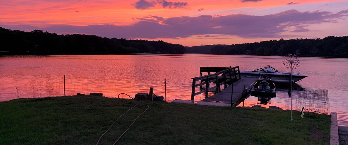 A sunset over a lake with a dock and a boat.