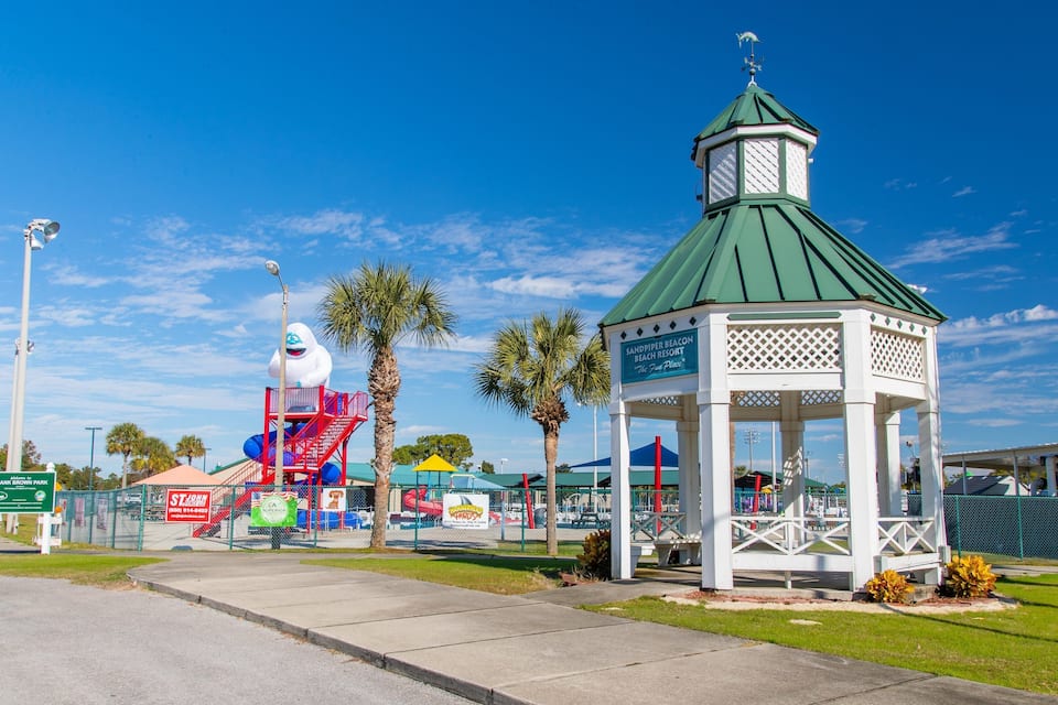 A park with a gazebo, palm trees, a rocket, and a playground.