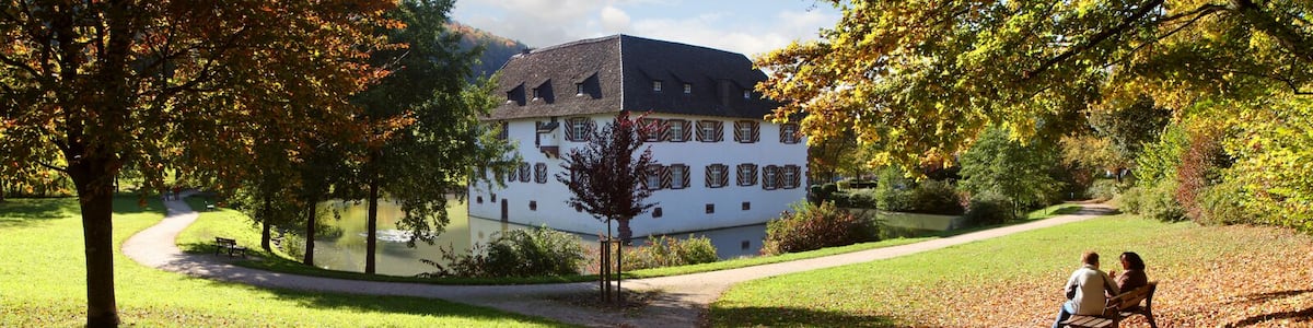 Un bâtiment blanc, doté d’un toit à forte pente, entouré d’arbres et bordé d’un sentier.