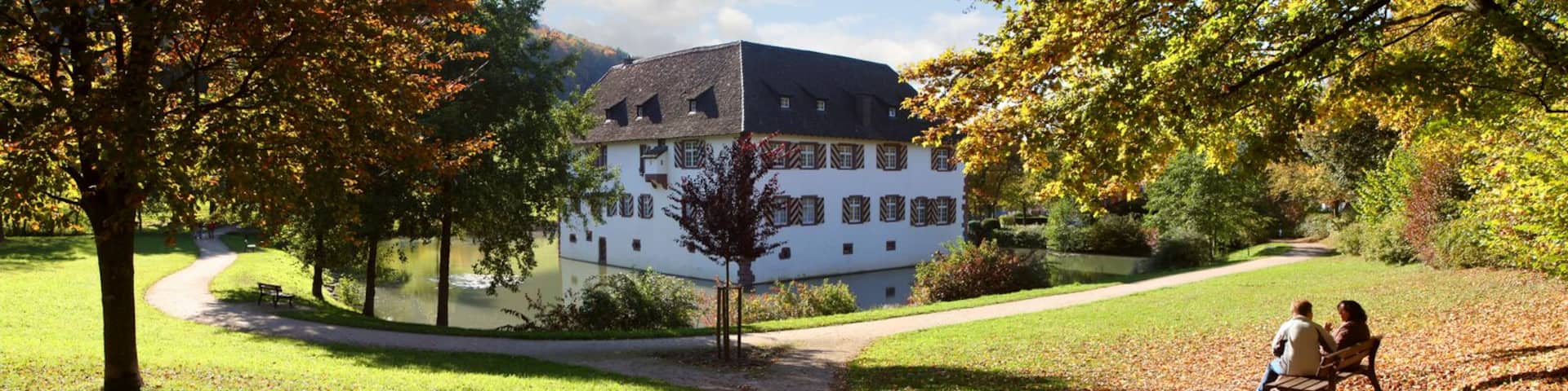 A white building with a steep roof, surrounded by trees and a pathway.