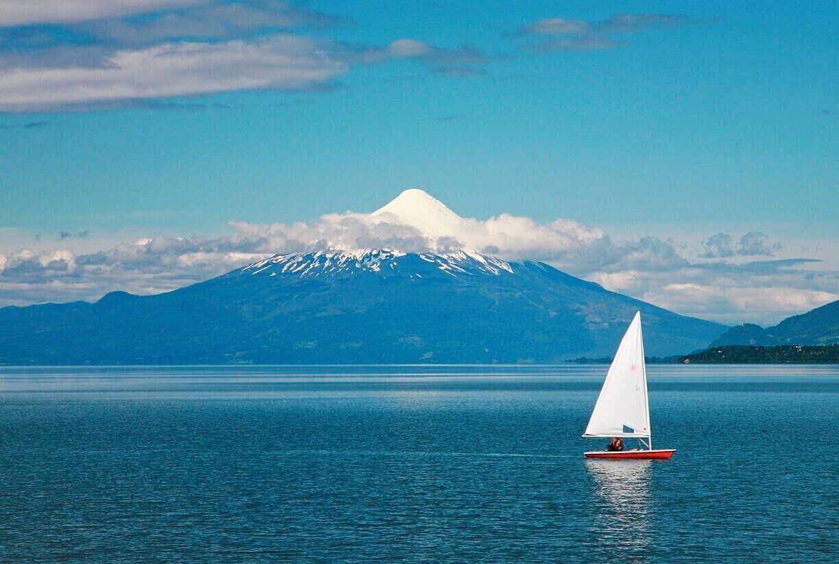 Un velero en aguas tranquilas, con una montaña nevada al fondo.