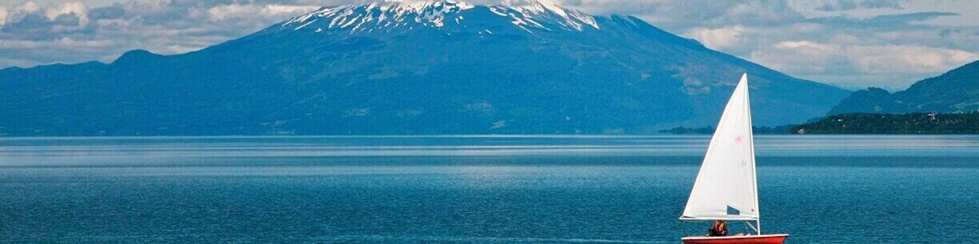 A sailboat on calm water with a snow-capped mountain in the background.