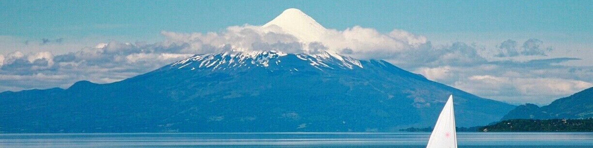 Un velero en aguas tranquilas, con una montaña nevada al fondo.