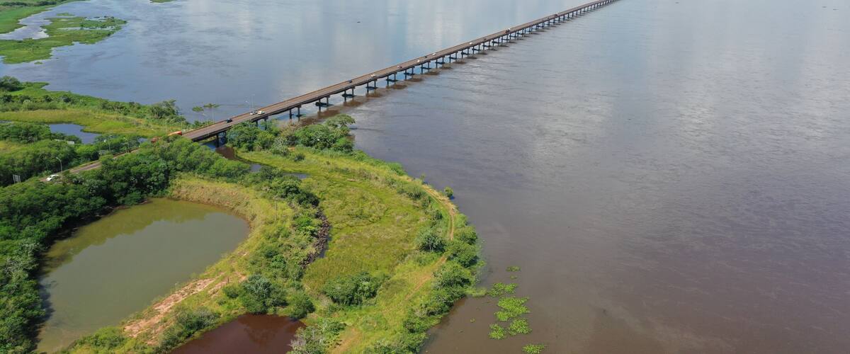 A long bridge over a wide river with green banks and small ponds.