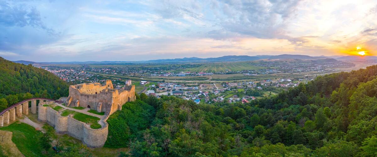 A historic castle surrounded by lush green hills and a small town in the valley below.