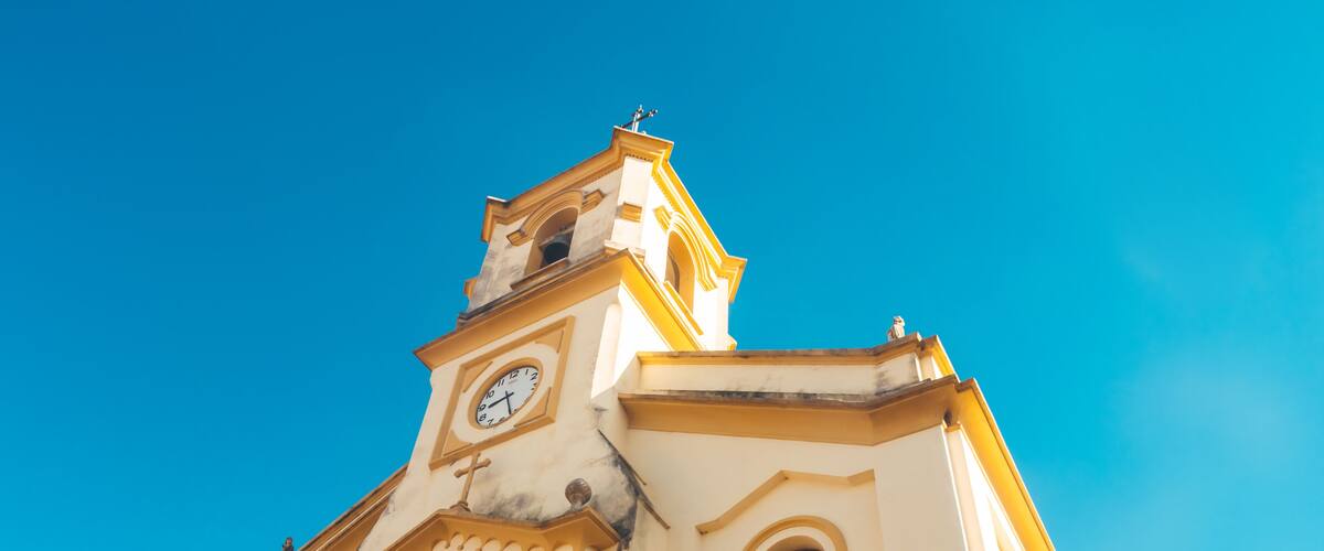 A church with a clock tower and arched windows against a clear blue sky.