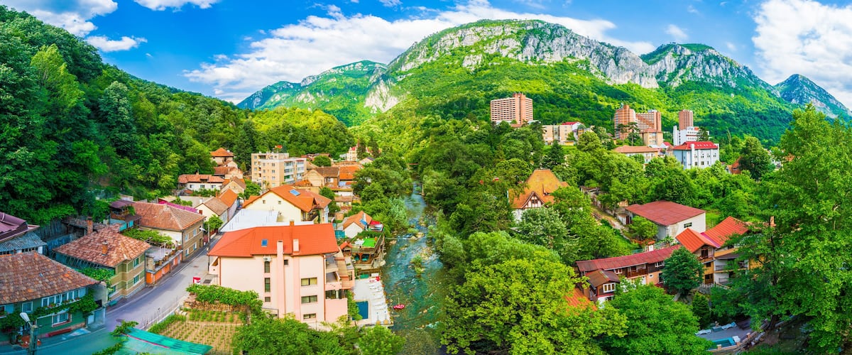 A town nestled in a valley with a river, surrounded by lush green mountains and red-roofed buildings.