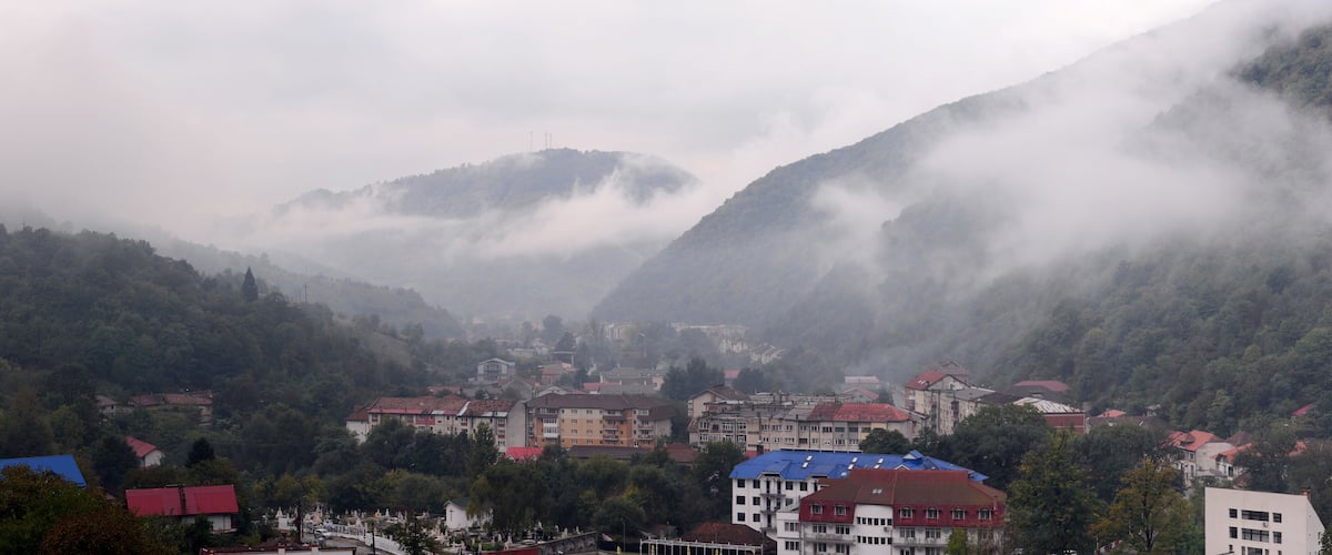 A town nestled in a valley with mountains in the background and mist covering the peaks.