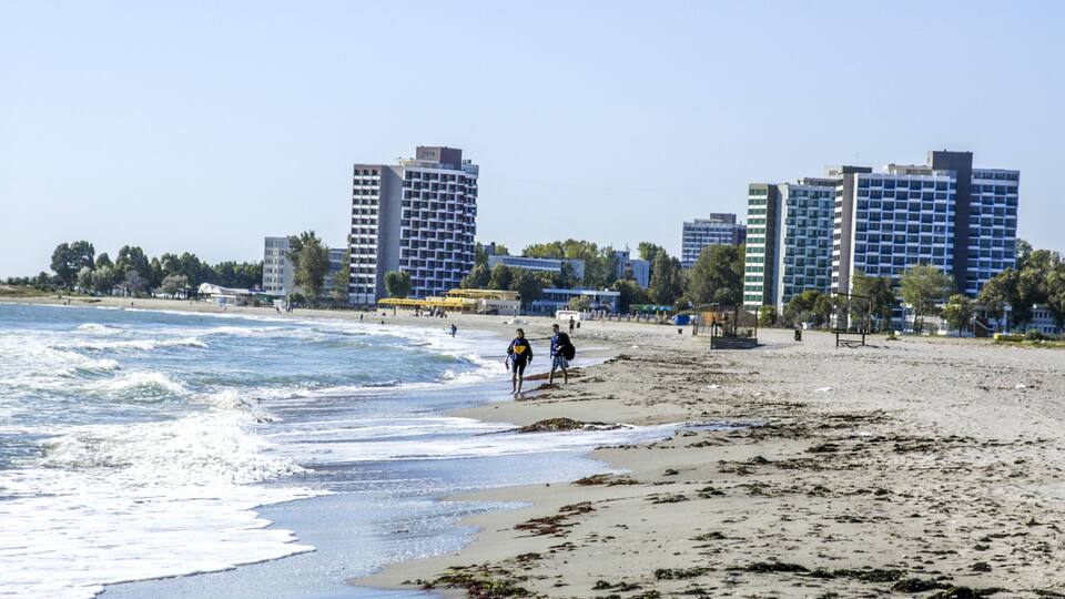A beach with waves, a sandy shore, and tall buildings in the background.