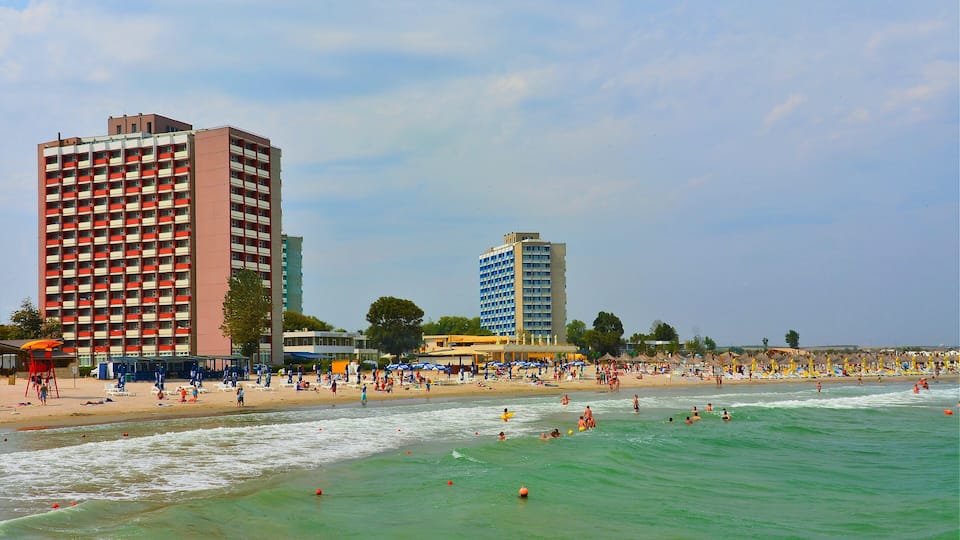 A beach with people swimming and sunbathing, a lifeguard tower, and tall buildings in the background.