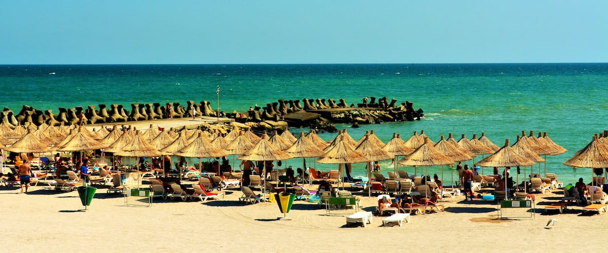 A beach with thatched umbrellas and lounge chairs.