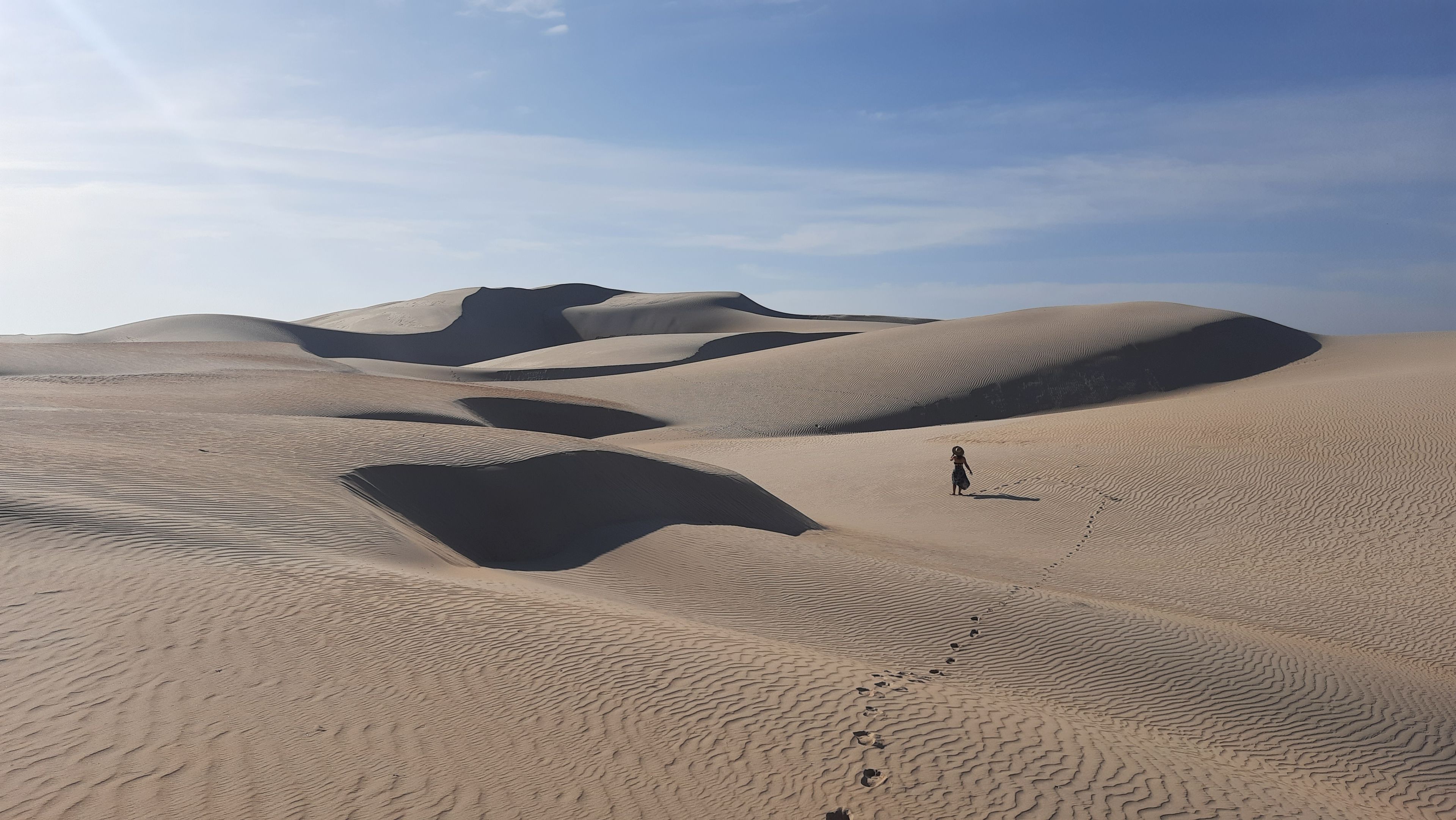 A desert landscape with sand dunes and a person walking.