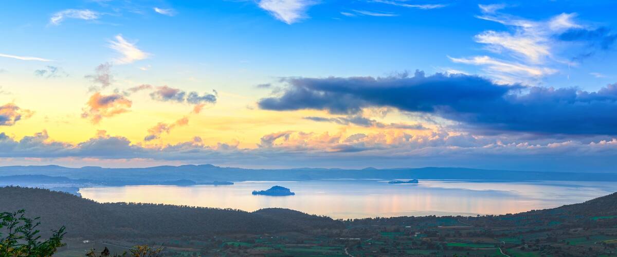 A panoramic view of a lake surrounded by hills and a village.