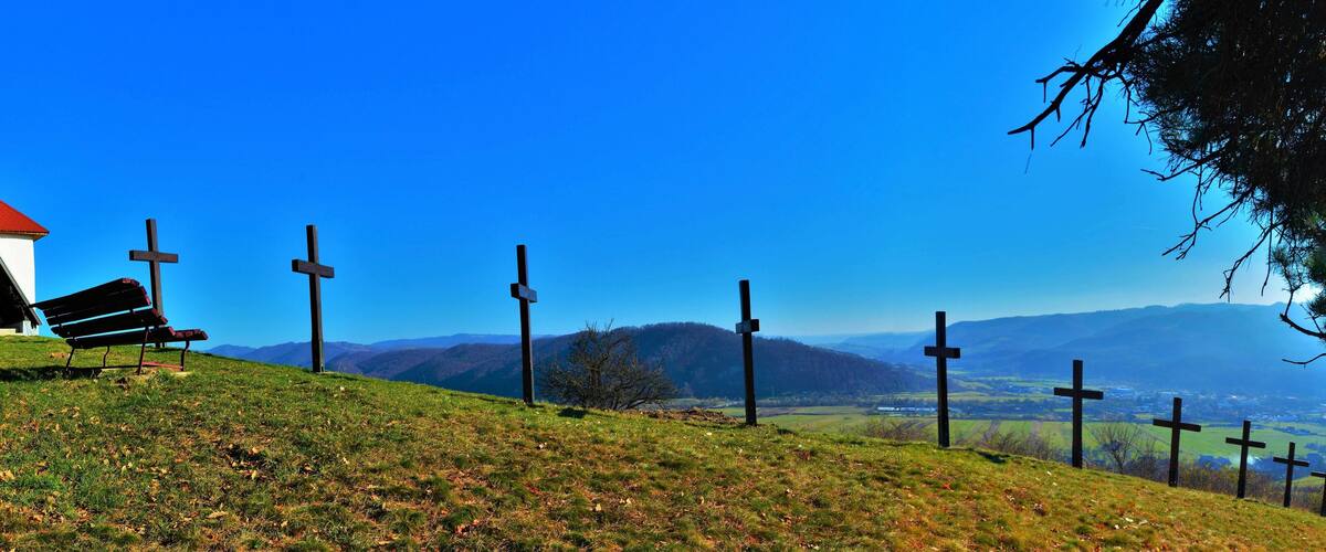 A church with a red roof and a cross on top, surrounded by a grassy hill with several crosses in the background.