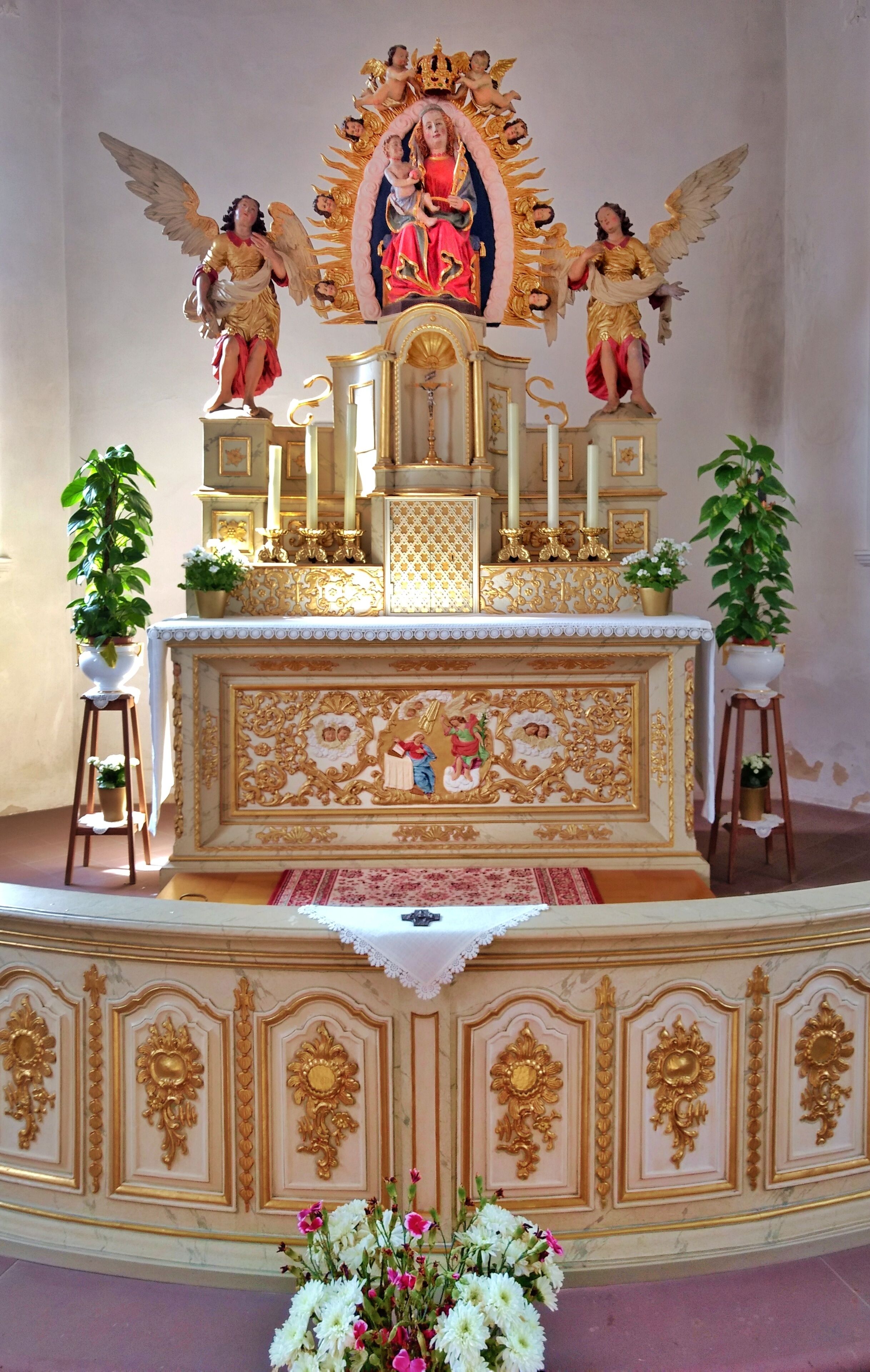 Un altar religioso ornamentado con decoraciones doradas, estatuas de ángeles y una figura central sosteniendo a un niño.