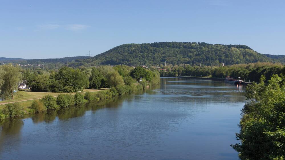 Ein Fluss mit einem Boot, umgeben von Grünflächen und Hügeln.
