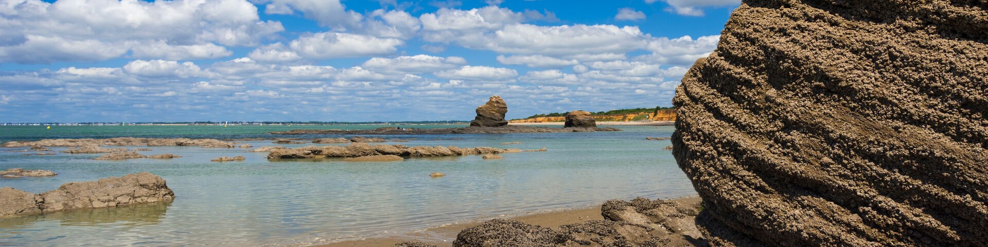 Paisagem costeira com águas azul-claras, formações rochosas e um penhasco imponente.