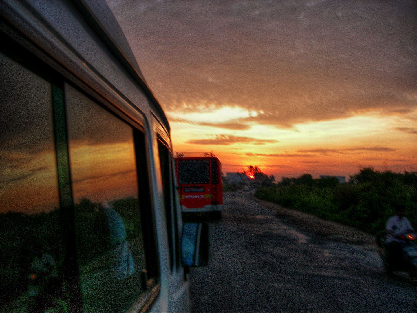 A sunset over a rural road with a bus and a motorcycle.