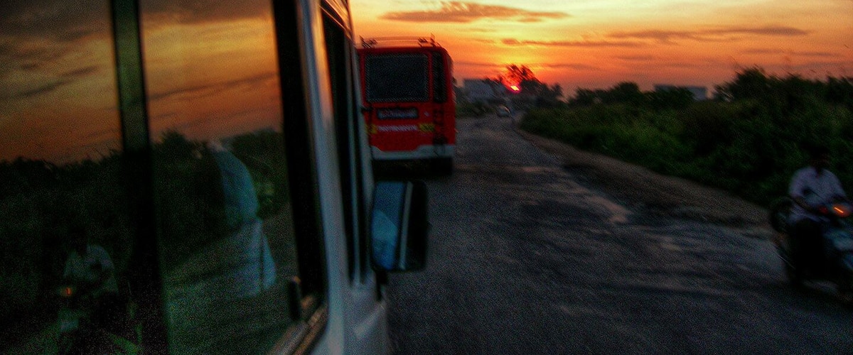 A sunset over a rural road with a bus and a motorcycle.