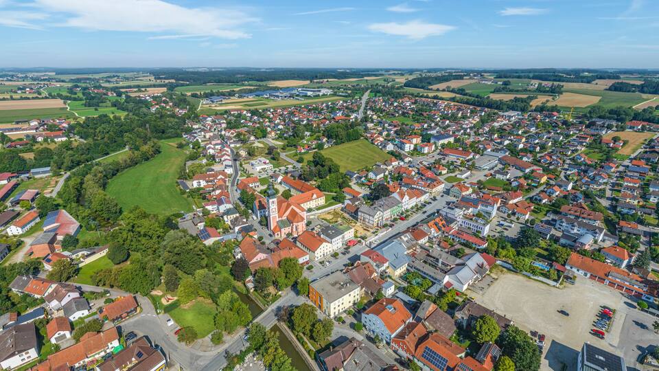 An aerial view of a small town with red-roofed houses, green fields, and a church.