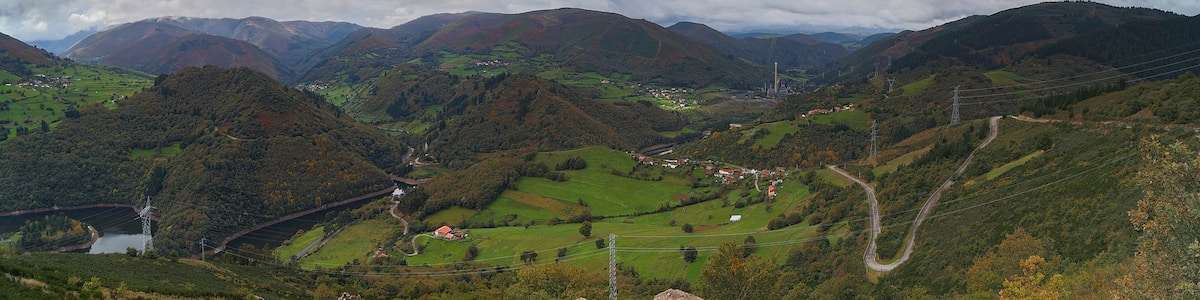 A mountainous landscape with a winding road, a small village, and a power line tower.