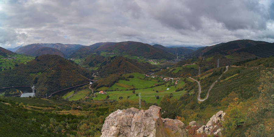 A mountainous landscape with a winding road, a small village, and a power line tower.