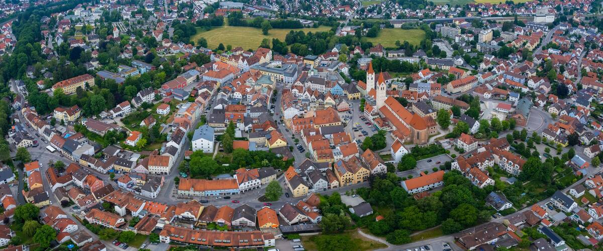 An aerial view of a historic town with a prominent church tower, surrounded by residential buildings and green spaces.