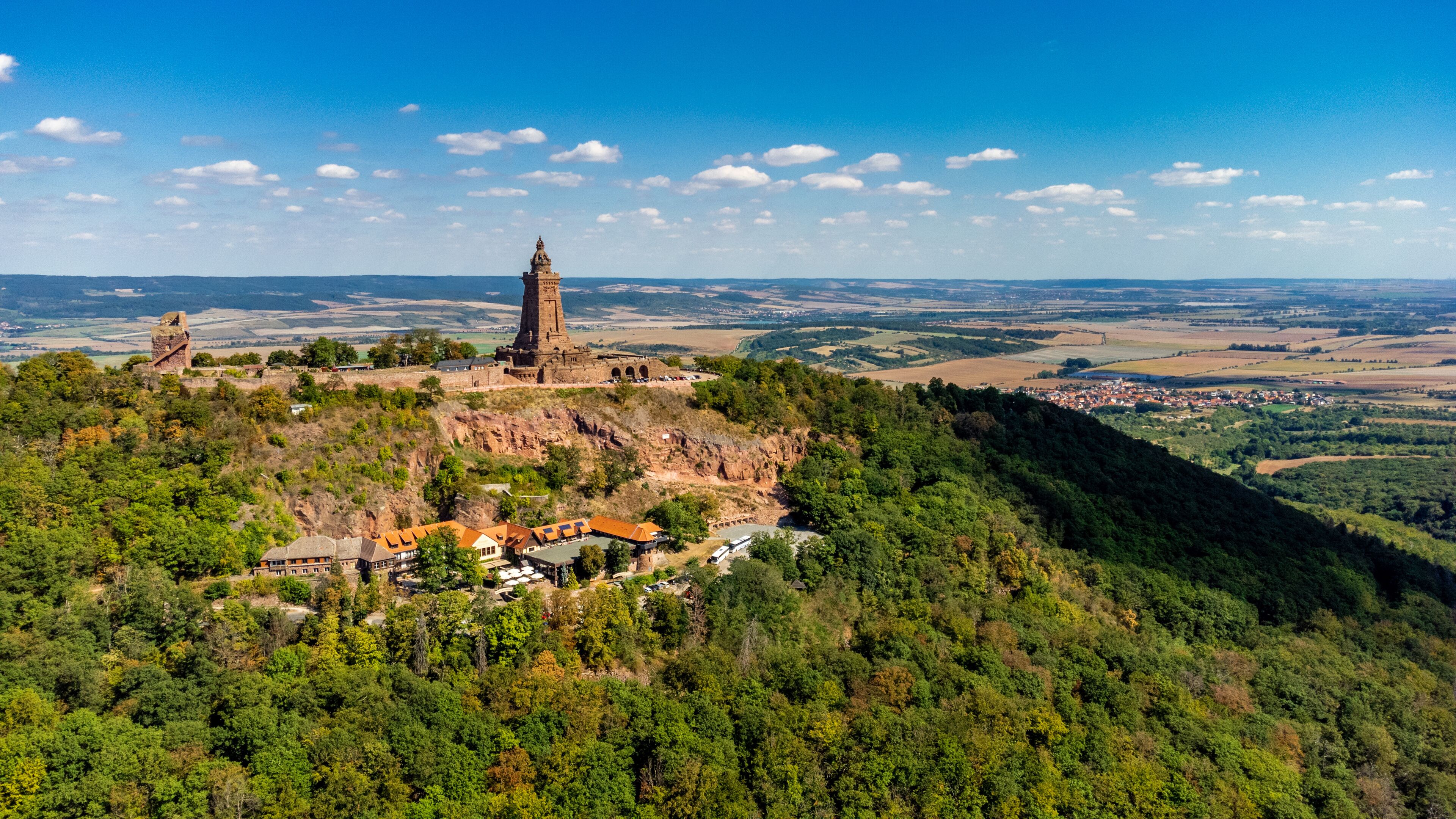A historic castle on a hill with a tower, surrounded by dense forest and a small village below.