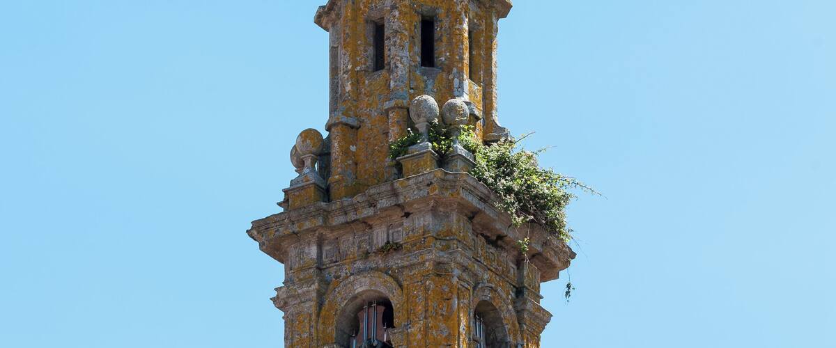 A historic bell tower with a weathered facade, a clock, and a cross on top.