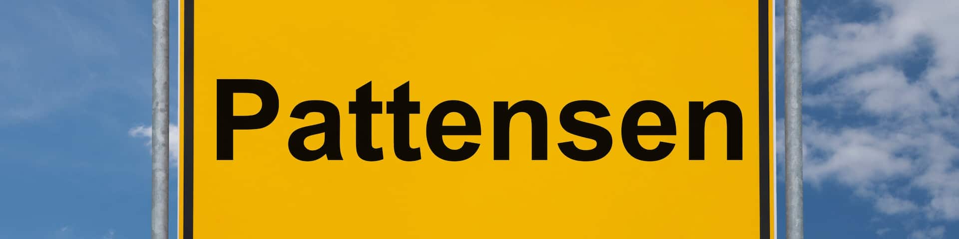 A yellow sign with the word "Pattensen" against a blue sky with clouds.