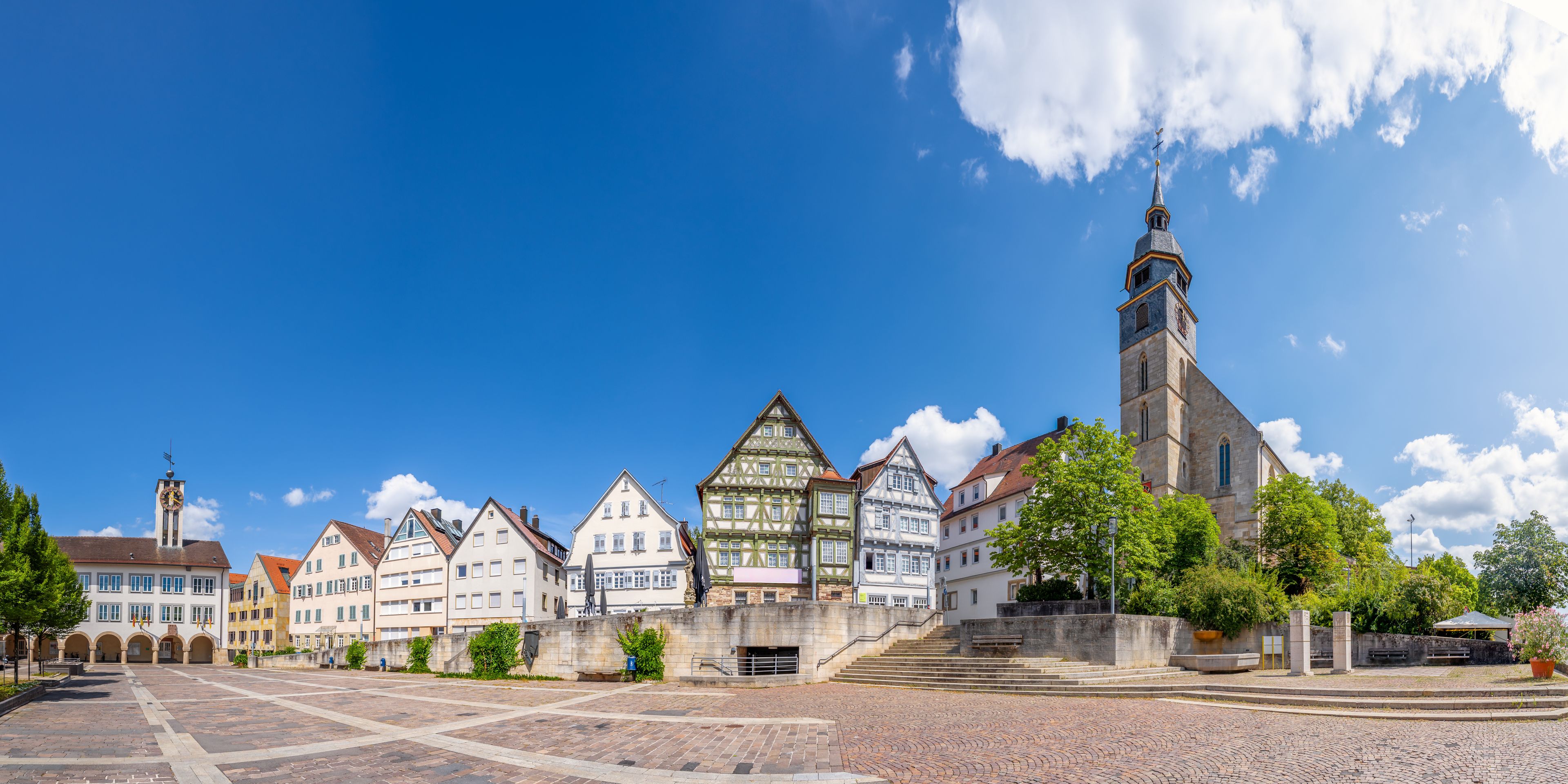 A historic town square with traditional half-timbered houses, a prominent church tower, and cobblestone streets.