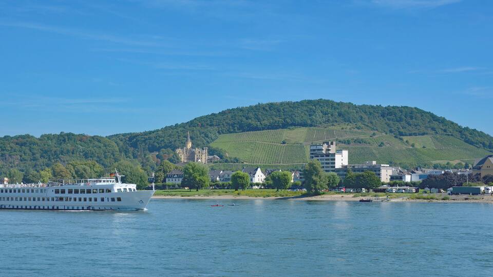 A river with a white boat, a hill with a castle, and a church with a tall spire.