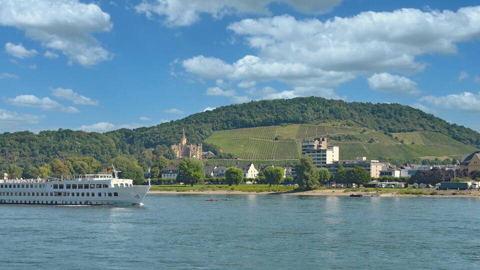 A river with a white boat, a church, and a castle on a hill.