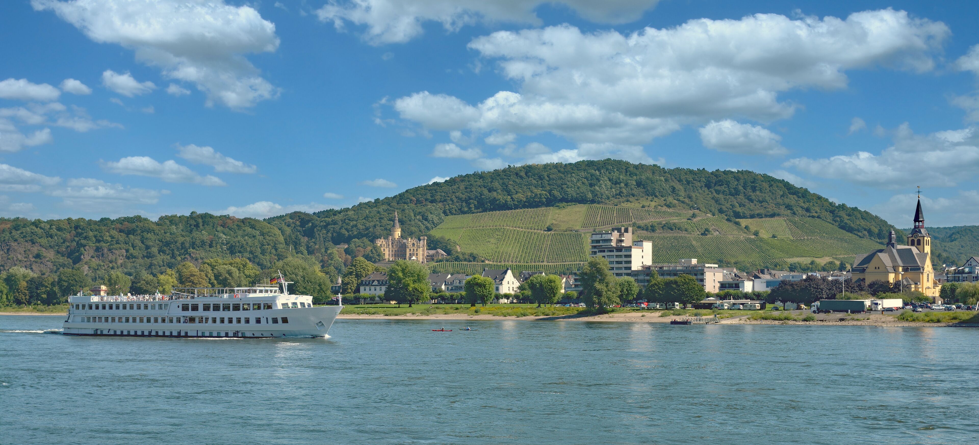 A river with a white boat, a church, and a castle on a hill.