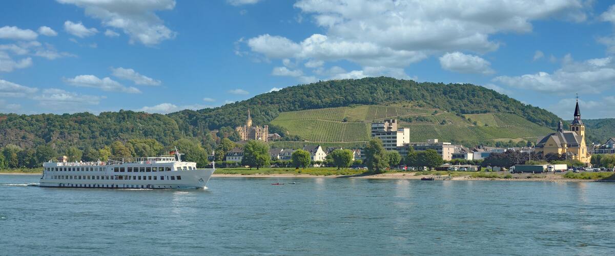 A river with a white boat, a church, and a castle on a hill.