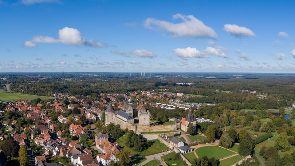 A town with historic architecture, wind turbines, and lush greenery.