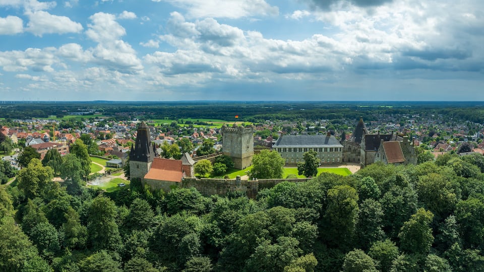 A historic town with a prominent castle, lush green surroundings, and a distant view of wind turbines.