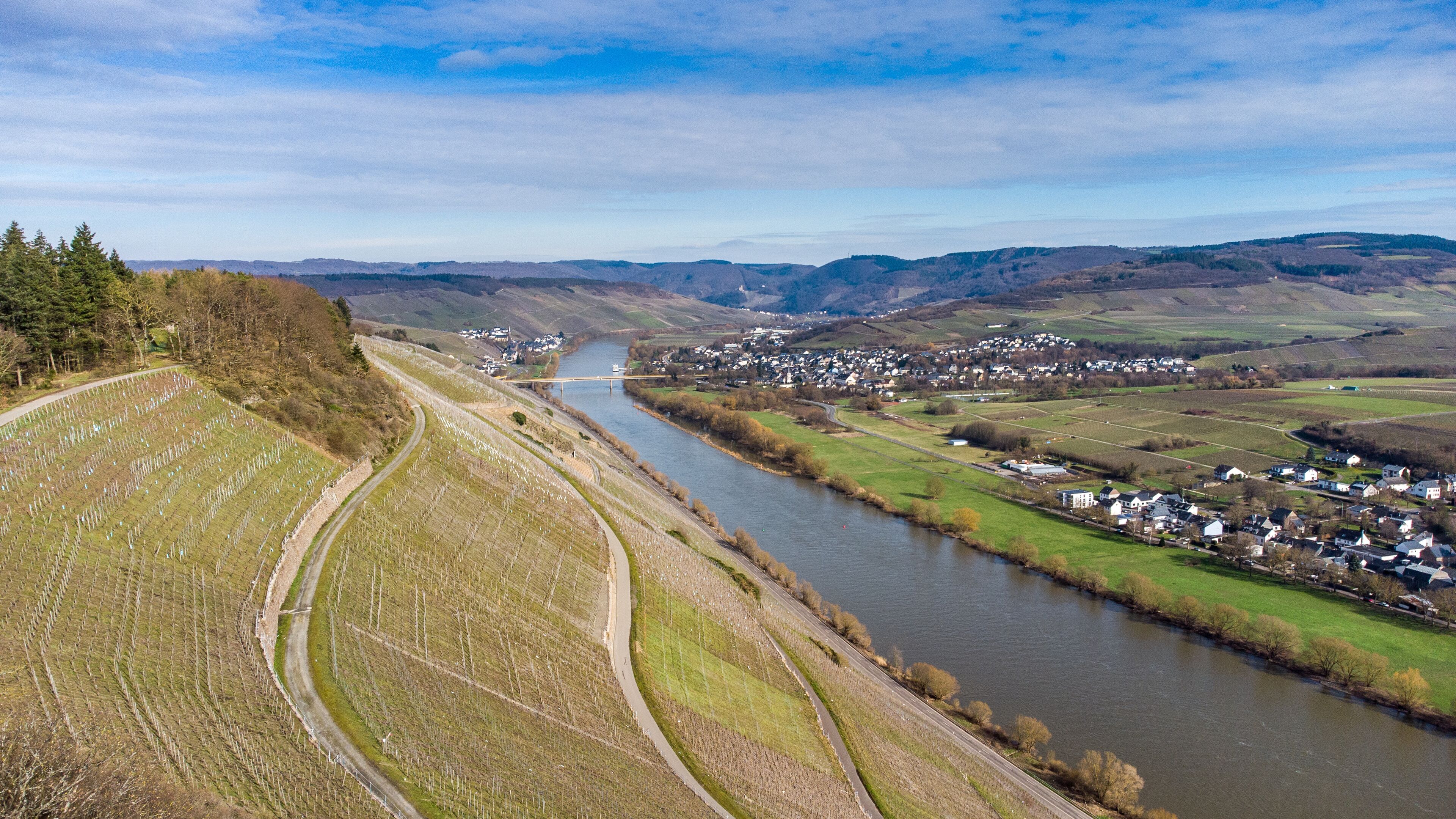 A river winding through a valley with a town on one side and a vineyard on the other.