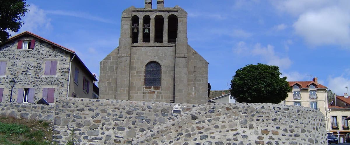 A stone church with a bell tower and a stone wall in front.