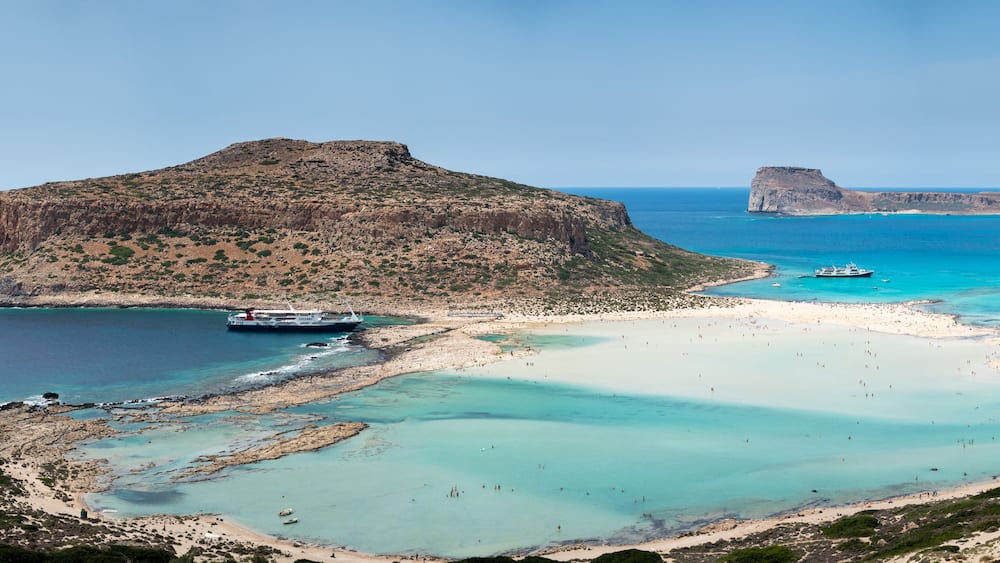 Eine Küstenlandschaft mit einer markanten Felseninsel, klarem türkisblauem Wasser und einem Sandstrand.