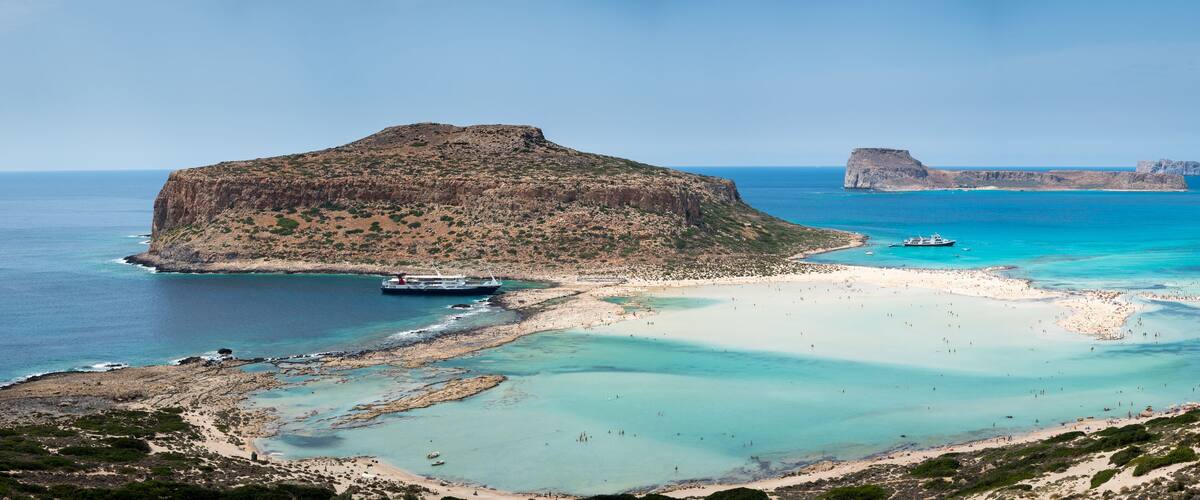 A coastal landscape with a prominent rocky island, clear turquoise waters, and a sandy beach.