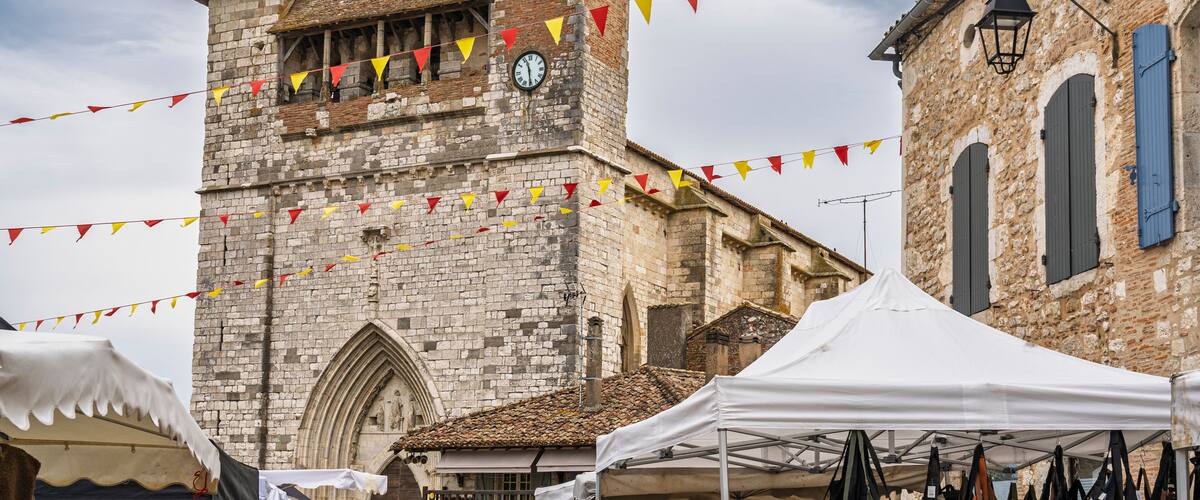 A historic stone church with a clock tower, surrounded by market stalls and a white tent.