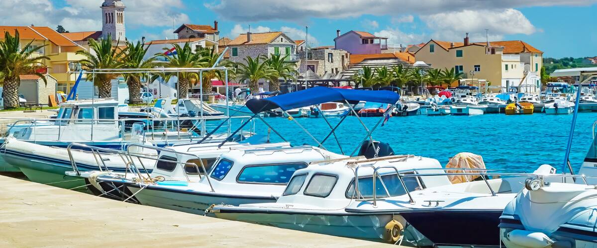 A marina with boats docked, a tower, and coastal buildings.