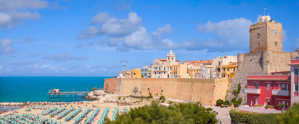A coastal town with a prominent tower, colorful buildings, and a beach with umbrellas.