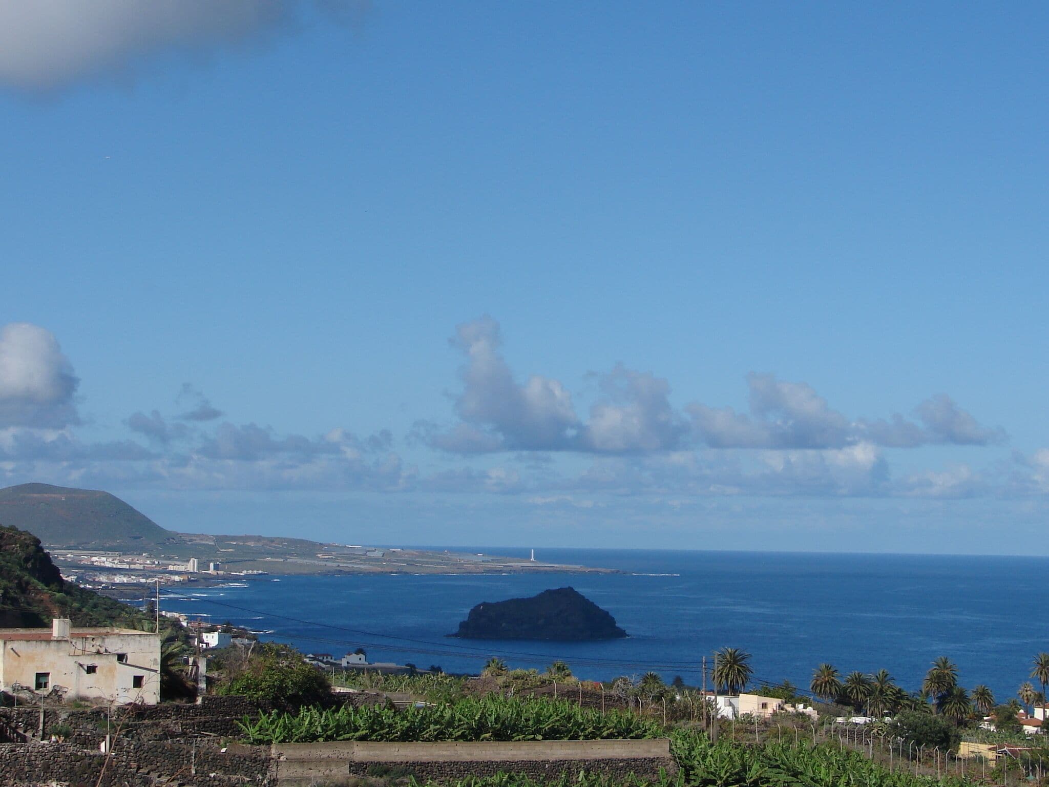 A coastal landscape with a prominent island, a lighthouse, and a distant cityscape.