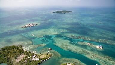 An aerial view of a tropical island with clear turquoise waters, a small settlement, and a distant larger island.